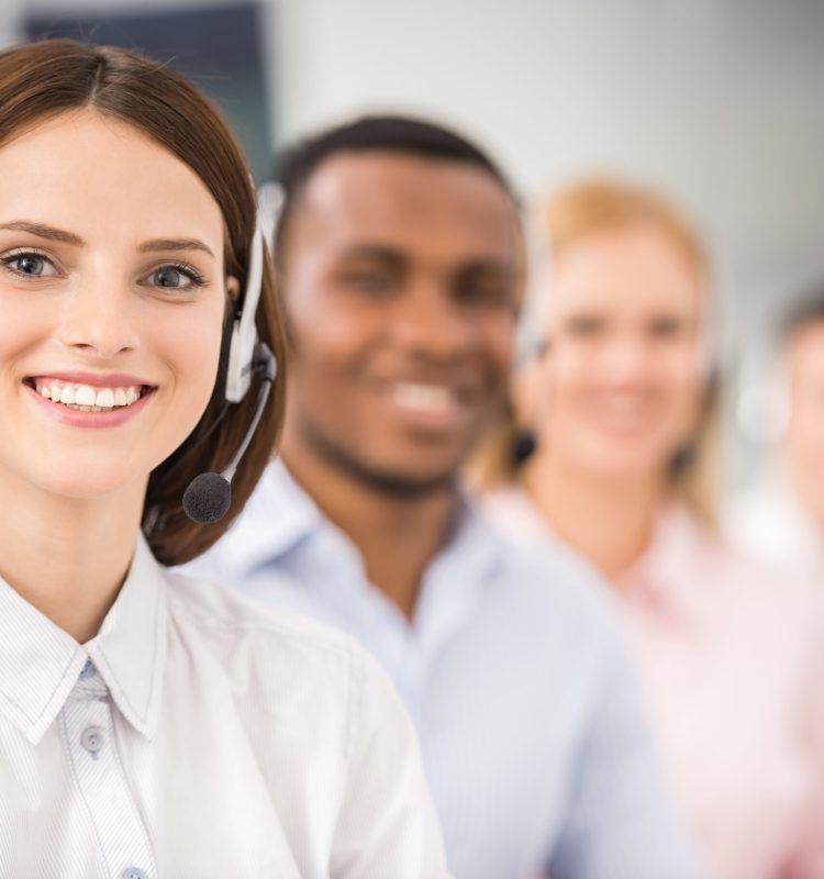 Smiling call center employees sitting in line with their headsets.